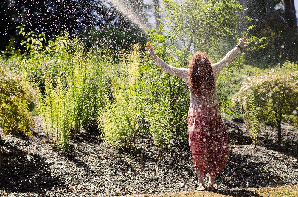 A woman dancing in water from a sprinkler in a garden.
Photo credit: Celeste Horrocks via Unsplash