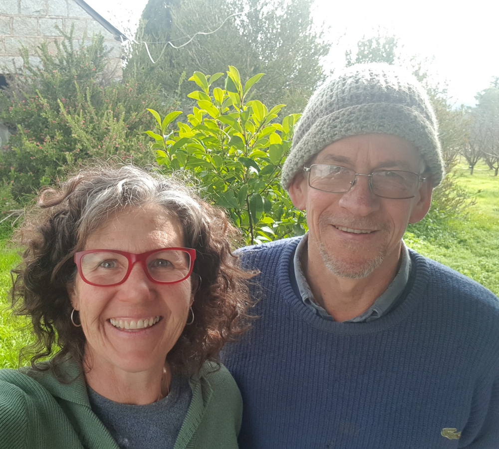 katie hugh rumpus room hat-1-1000x901 Woman with curly hair and red glasses next to a man with a blue jumper and grey hat in front of a granite building and trees